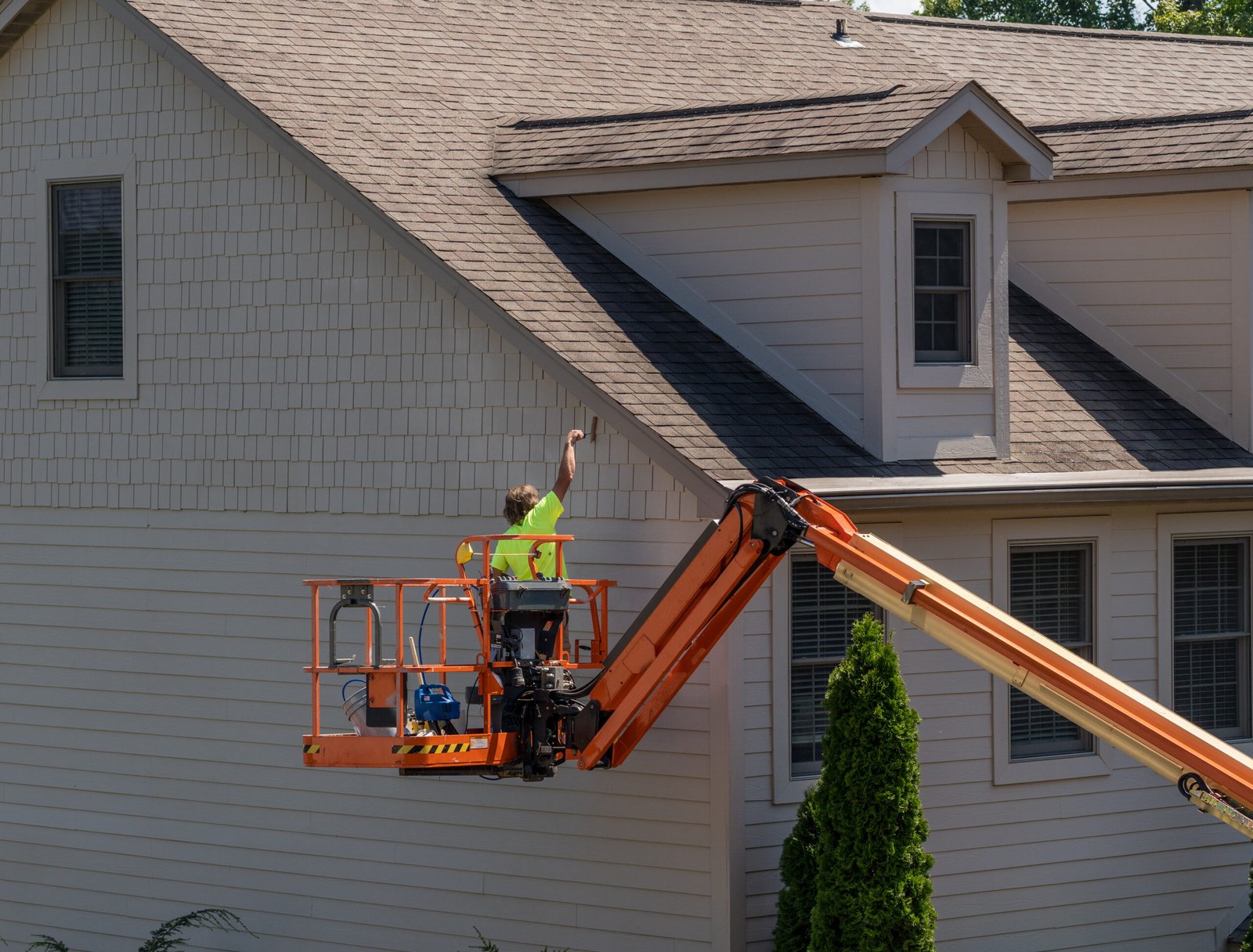 Professional painter on a lift painting the exterior siding of a house in Northern Kentucky. Pillar Painting & Contracting
